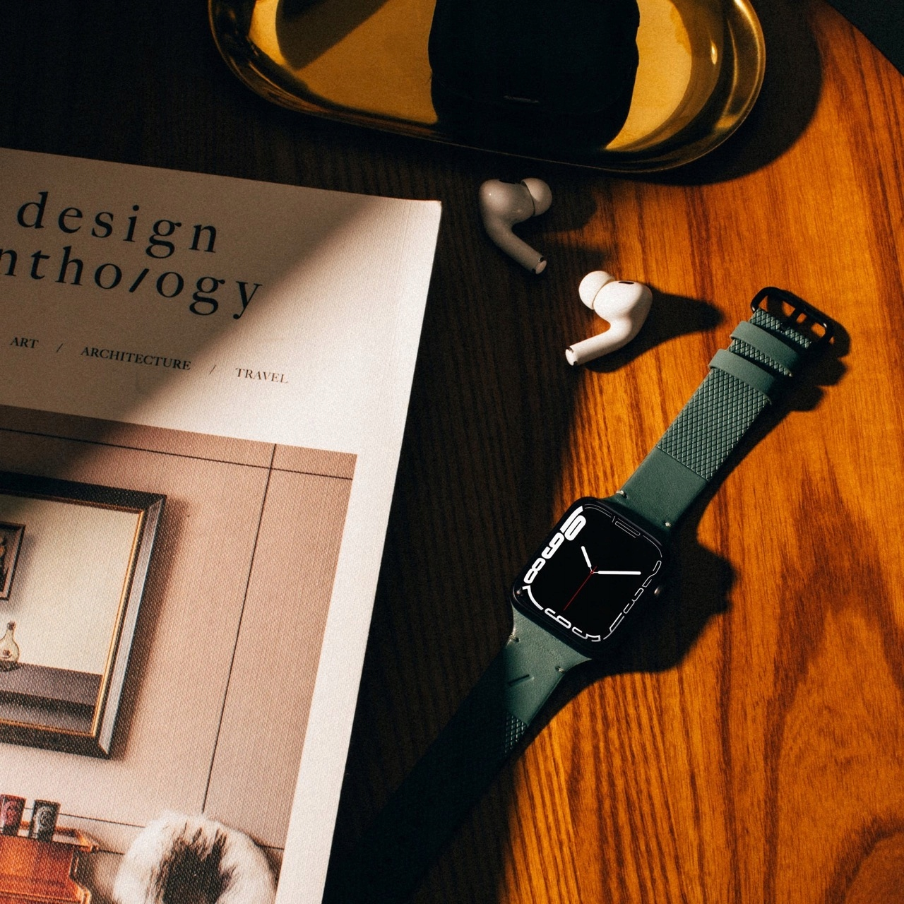 Zielony smartwatch, białe słuchawki i magazyn na drewnianym stole.
