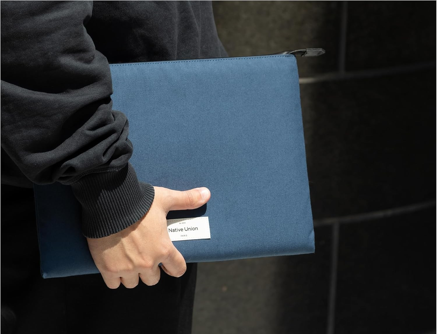 Una persona tiene una borsa blu scuro. A sinistra si vede una felpa nera.