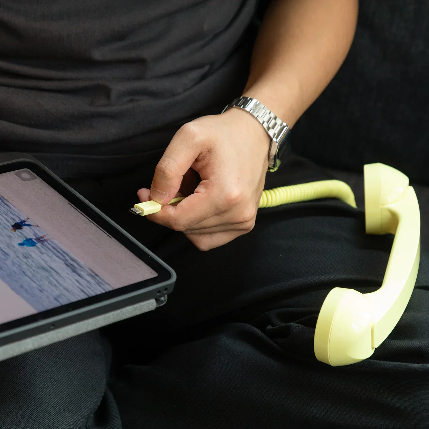 Una mano tiene un cavo giallo che si collega a un tablet, con una cornetta retrò nelle vicinanze.