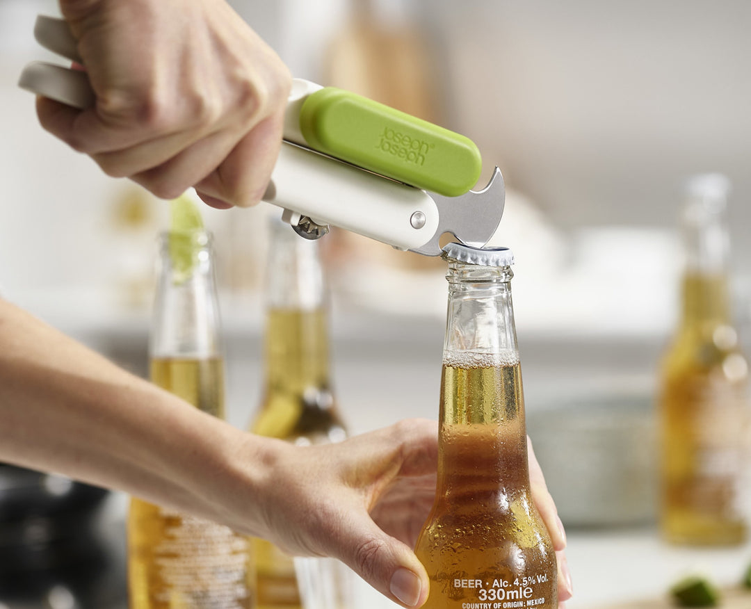 Hände öffnen eine Bierflasche mit einem Joseph Joseph Öffner. Zwei weitere Flaschen im Hintergrund.