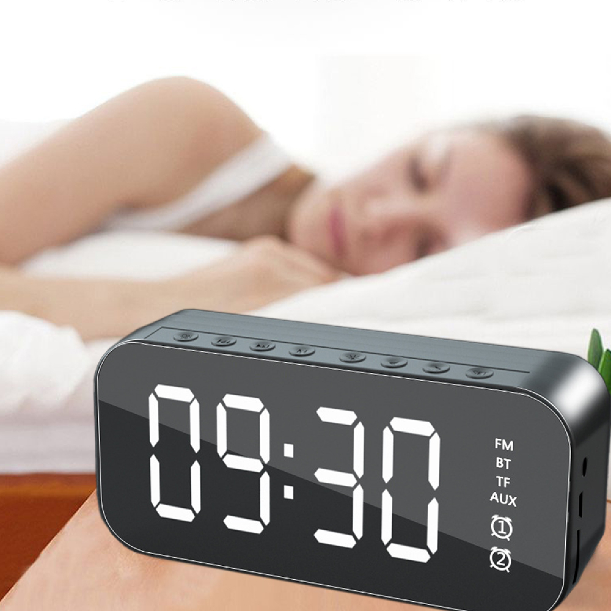 Ein schwarzer Digitalwecker mit hellen Ziffern zeigt 09:30 an. Eine Person schläft im Hintergrund.