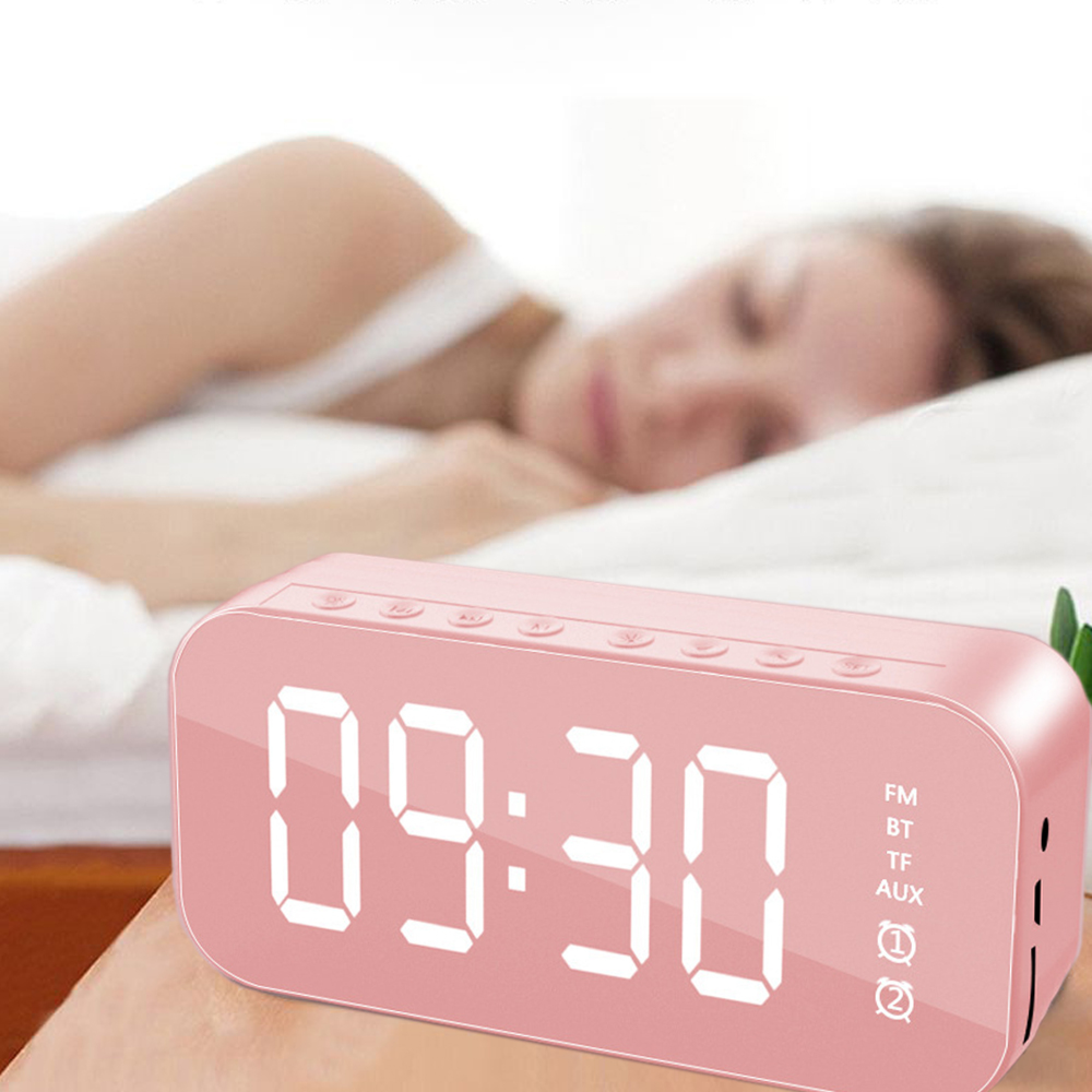 Ein rosafarbener Digitalwecker zeigt 09:30 an, eine Person schläft im Hintergrund.