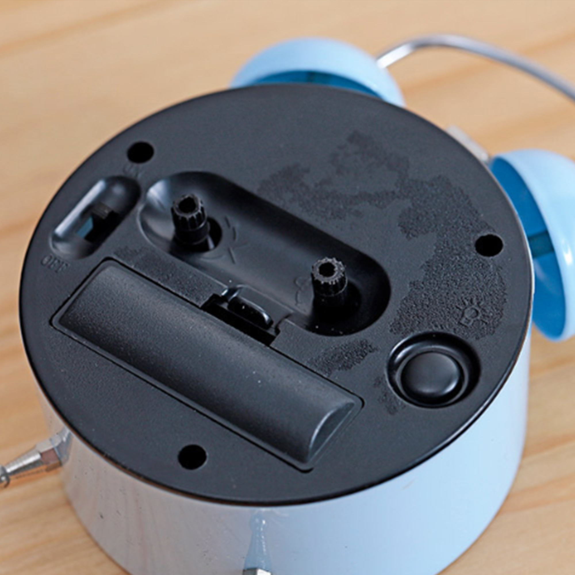 Unterseite eines hellblauen Weckers mit Batteriefach und Schaltern.