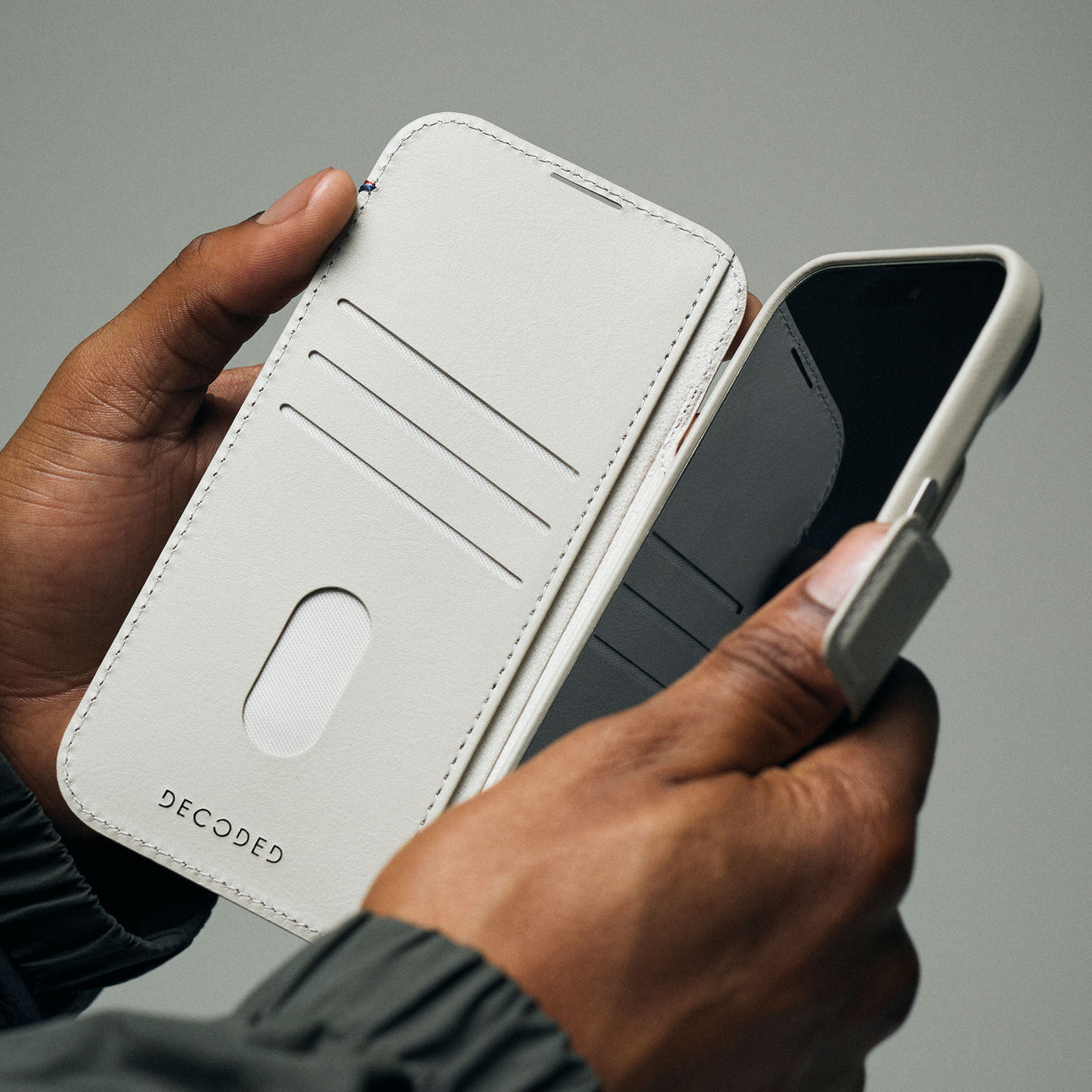 Mani tengono un telefono grigio chiaro con custodia a portafoglio. L'interno ha slot per carte.