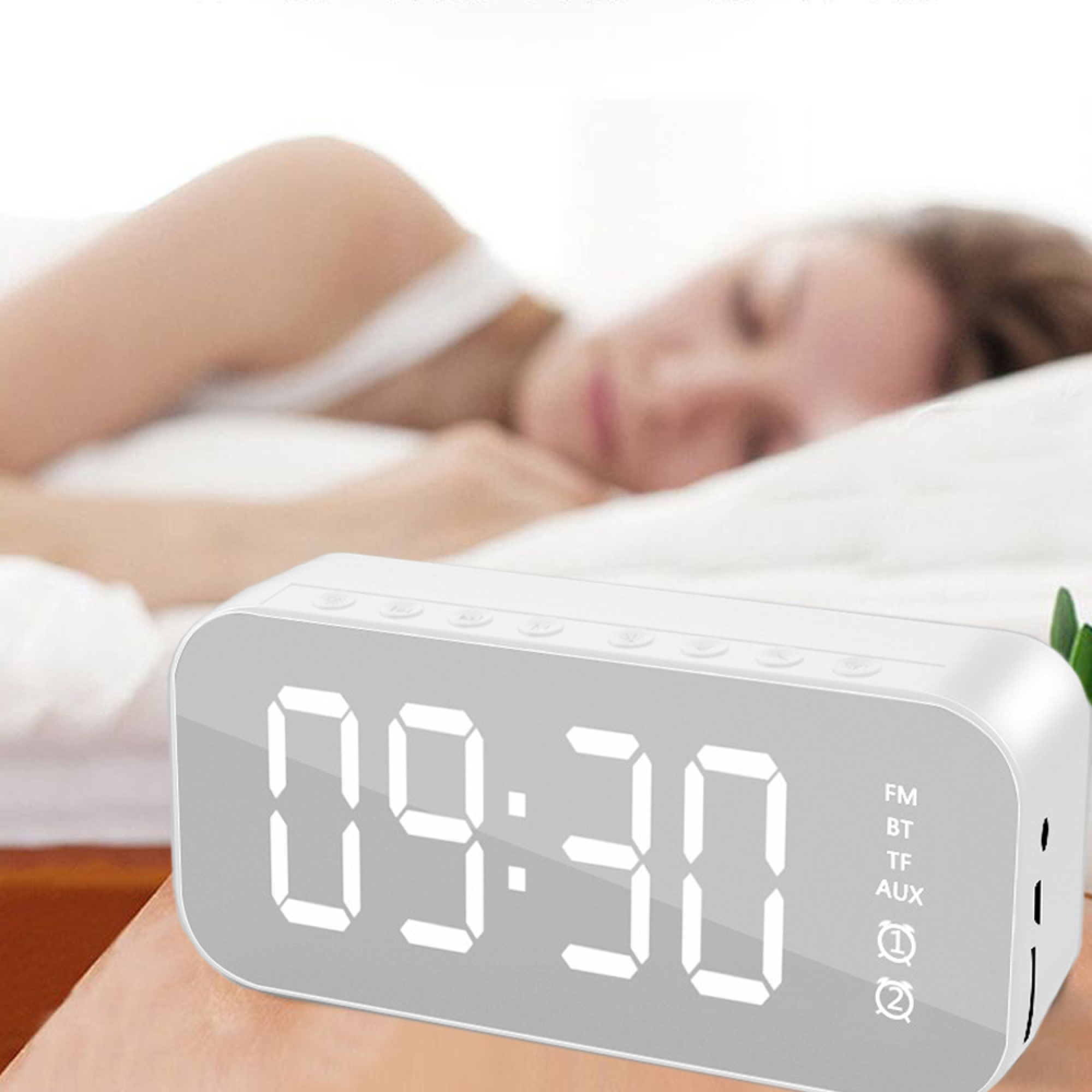 Ein weißer Digitalwecker zeigt 09:30 an. Eine Person schläft dahinter im Bett.