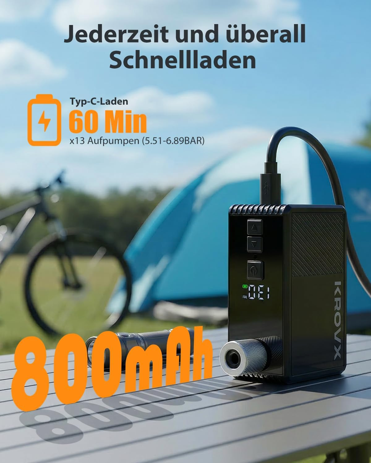 Schwarzer KROVX Luftkompressor auf Tisch mit Fahrrad & Zelt im Hintergrund.