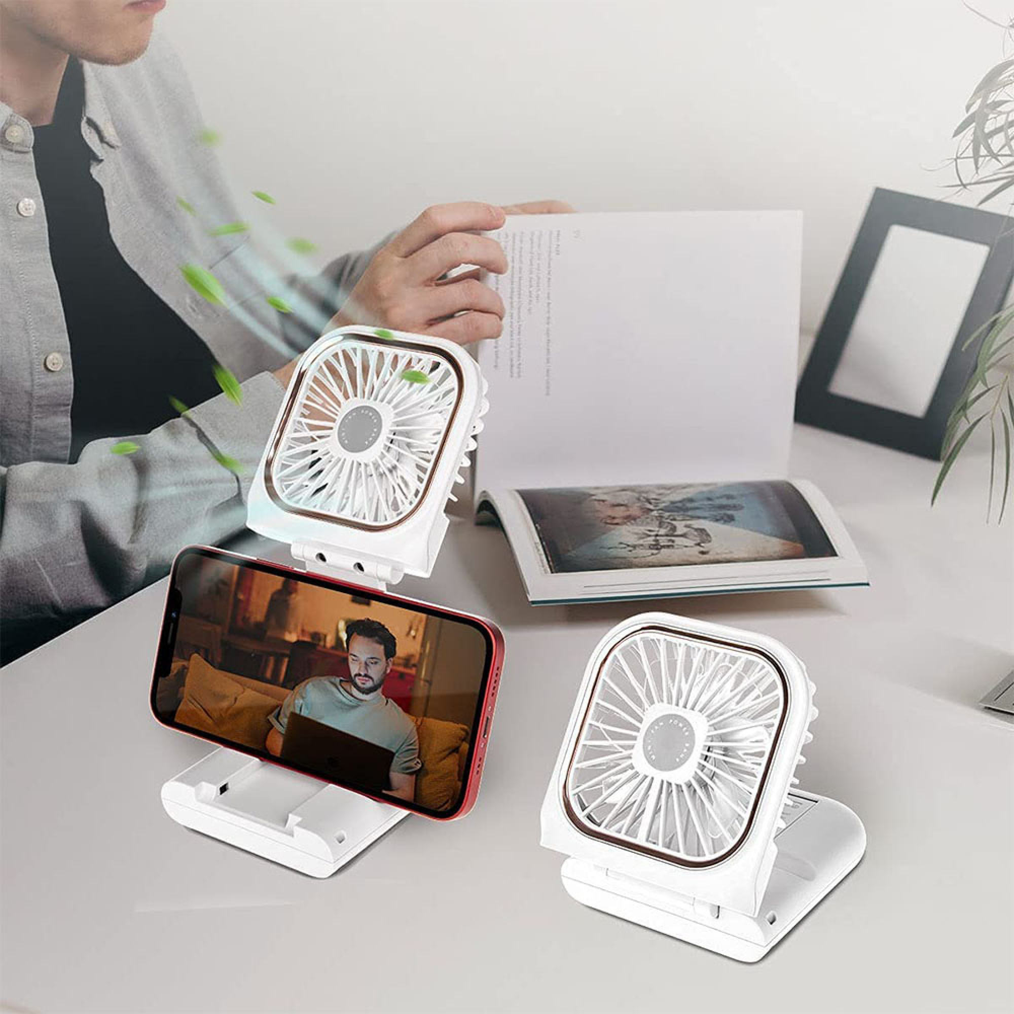 Zwei weiße Lüfter, ein Smartphone mit Mann auf dem Bildschirm, ein Buch, ein Mann liest.