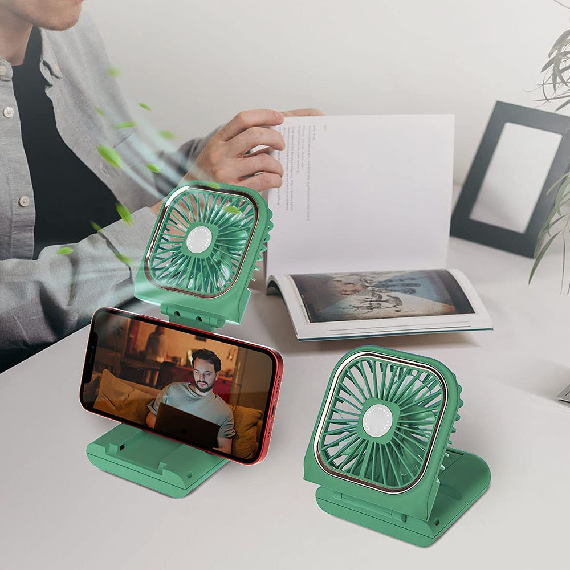 Grüne Mini-Ventilatoren stehen auf einem Schreibtisch, einer hält ein Handy.