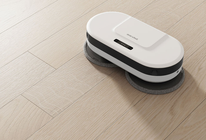 Ein weißer Roboterreiniger mit schwarzen Akzenten auf einem hellen Holzboden.