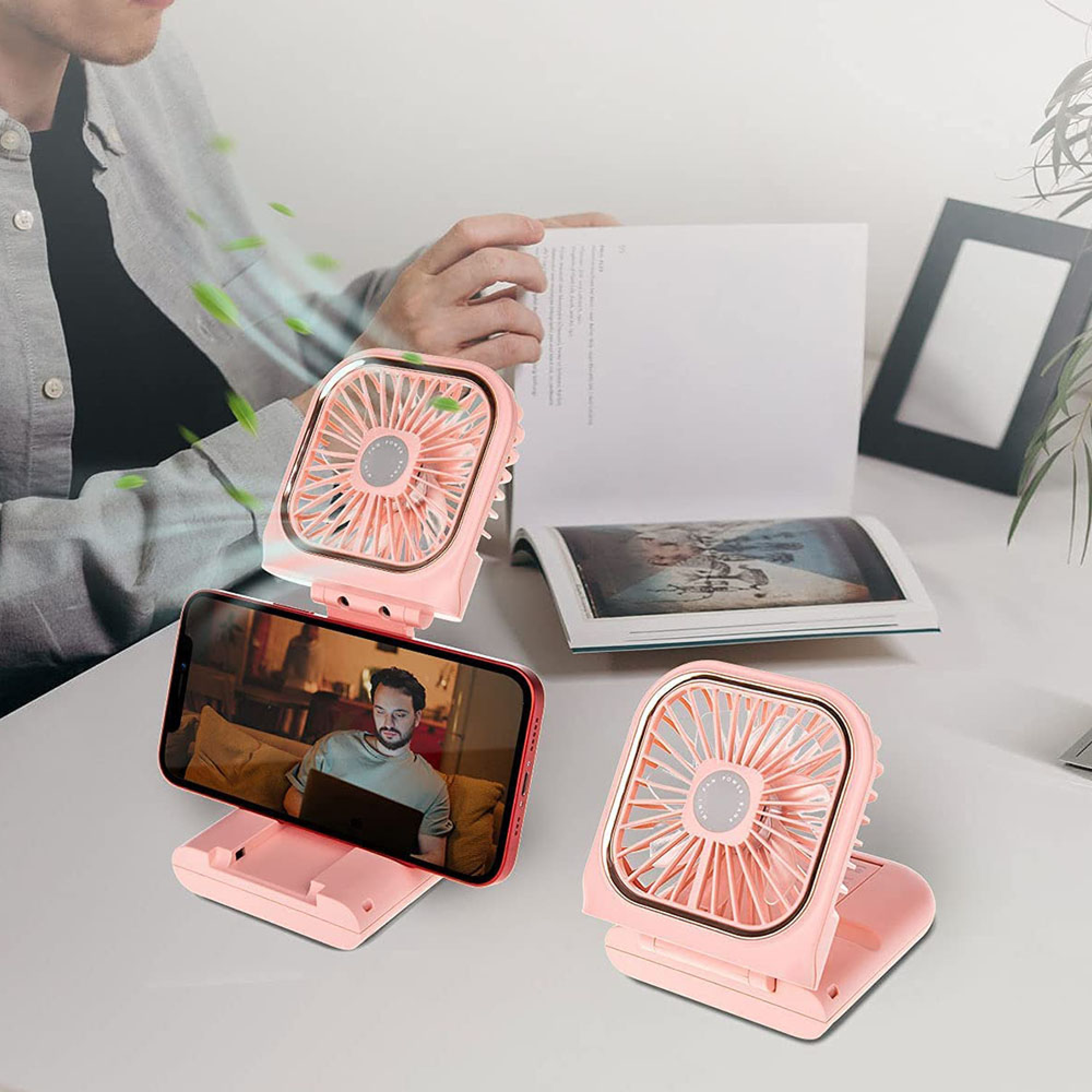 Rosa Lüfter und Handy auf einem Schreibtisch. Ein Mann liest.