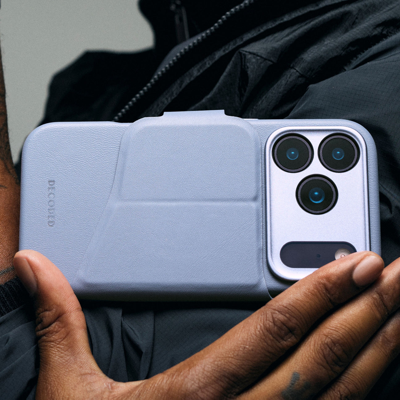 Custodia per telefono azzurra con array a tripla fotocamera tenuta da mani scure.