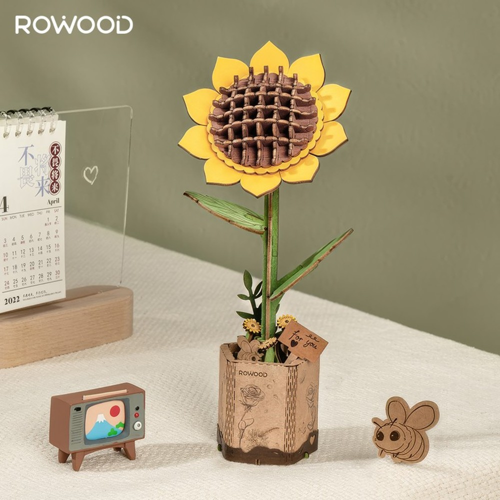 Un modèle de tournesol en bois, une mini-télévision, une abeille et un calendrier sur une table.