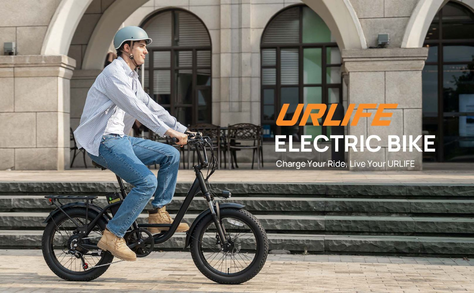 Hombre con casco monta una bicicleta eléctrica negra frente a un edificio.