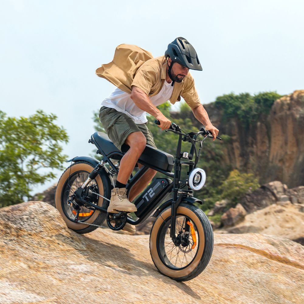 Uomo guida una e-bike nera con ruote grasse su terreno roccioso.