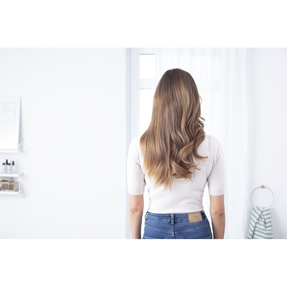 Rückansicht einer Frau mit langen, braunen Haaren in einem hellrosa Oberteil und blauen Jeans.