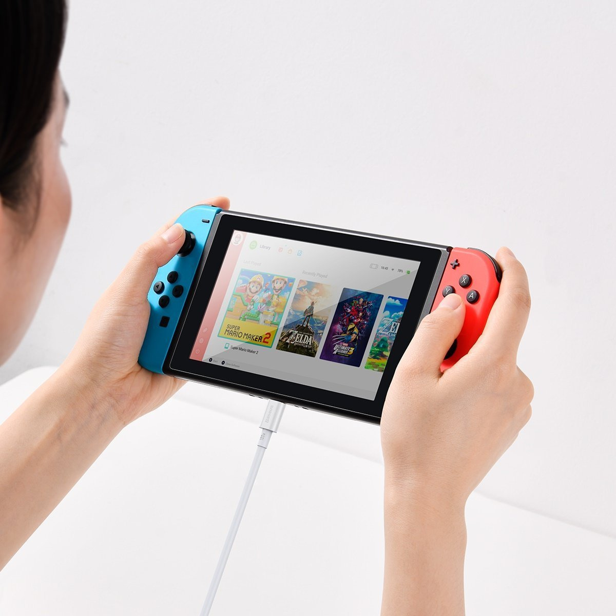 Person hält Nintendo Switch mit blauen und roten Joy-Cons, lädt mit weißem Kabel.