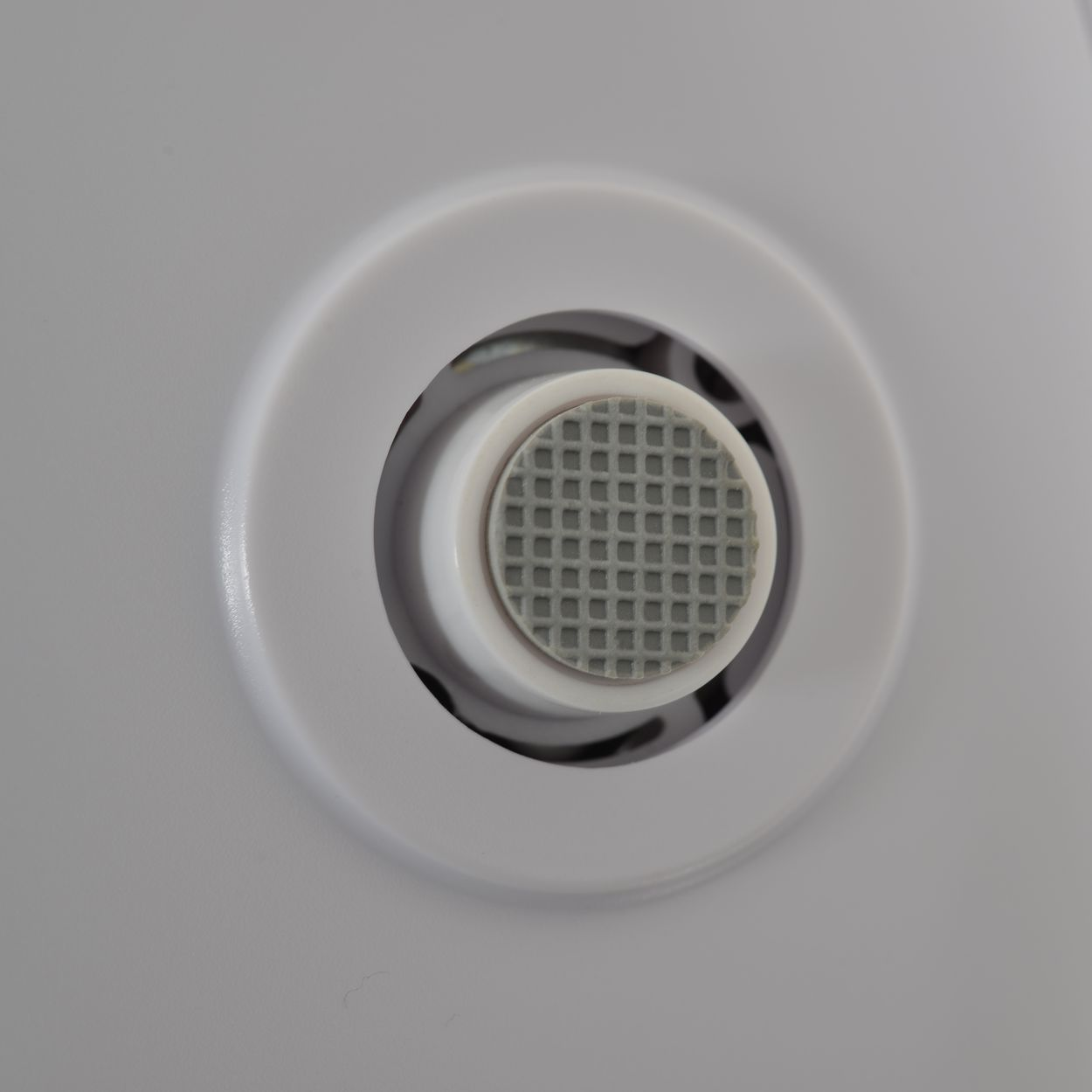 Grauer gerippter Knopf in einem weißen Kreis auf weißem Hintergrund.