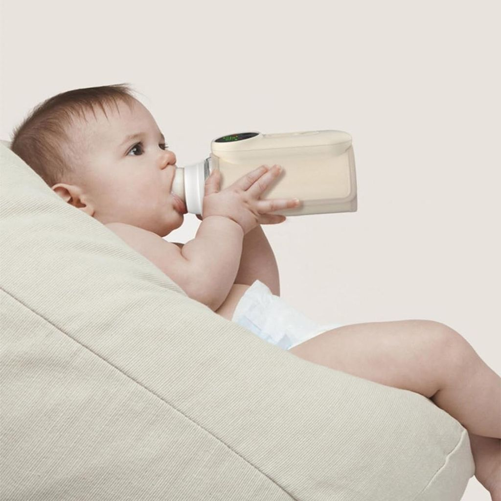 Baby trinkt aus Flasche auf hellem Kissen sitzend.