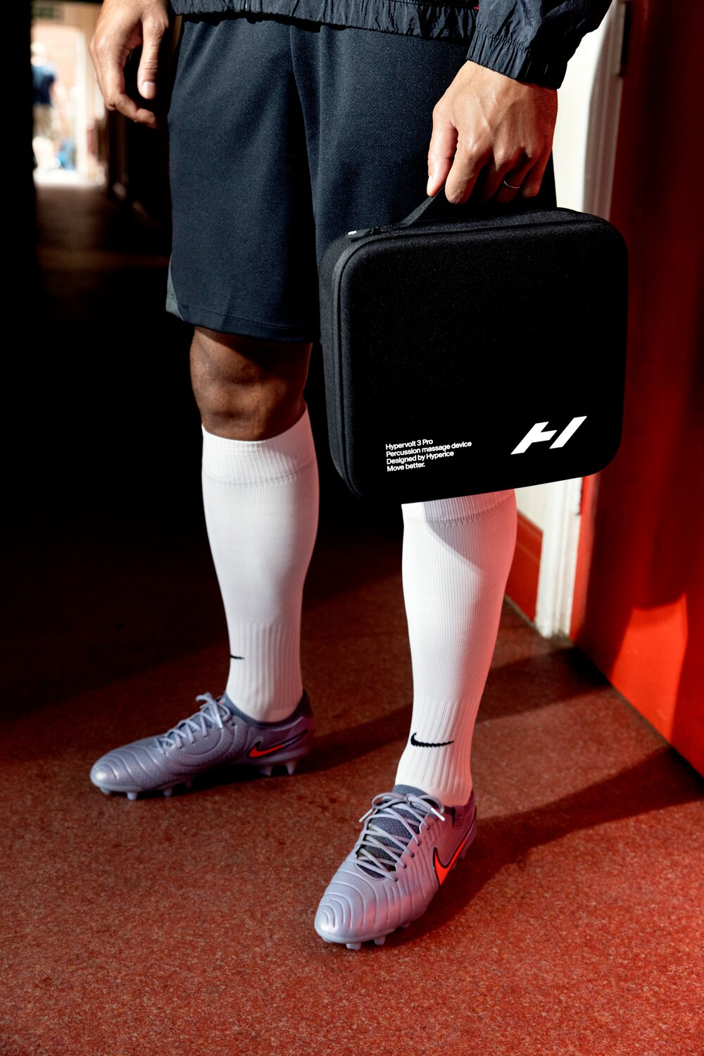 Ein Mann in Fußballkleidung hält eine schwarze Tasche mit der Aufschrift Hypervolt 3 Pro.