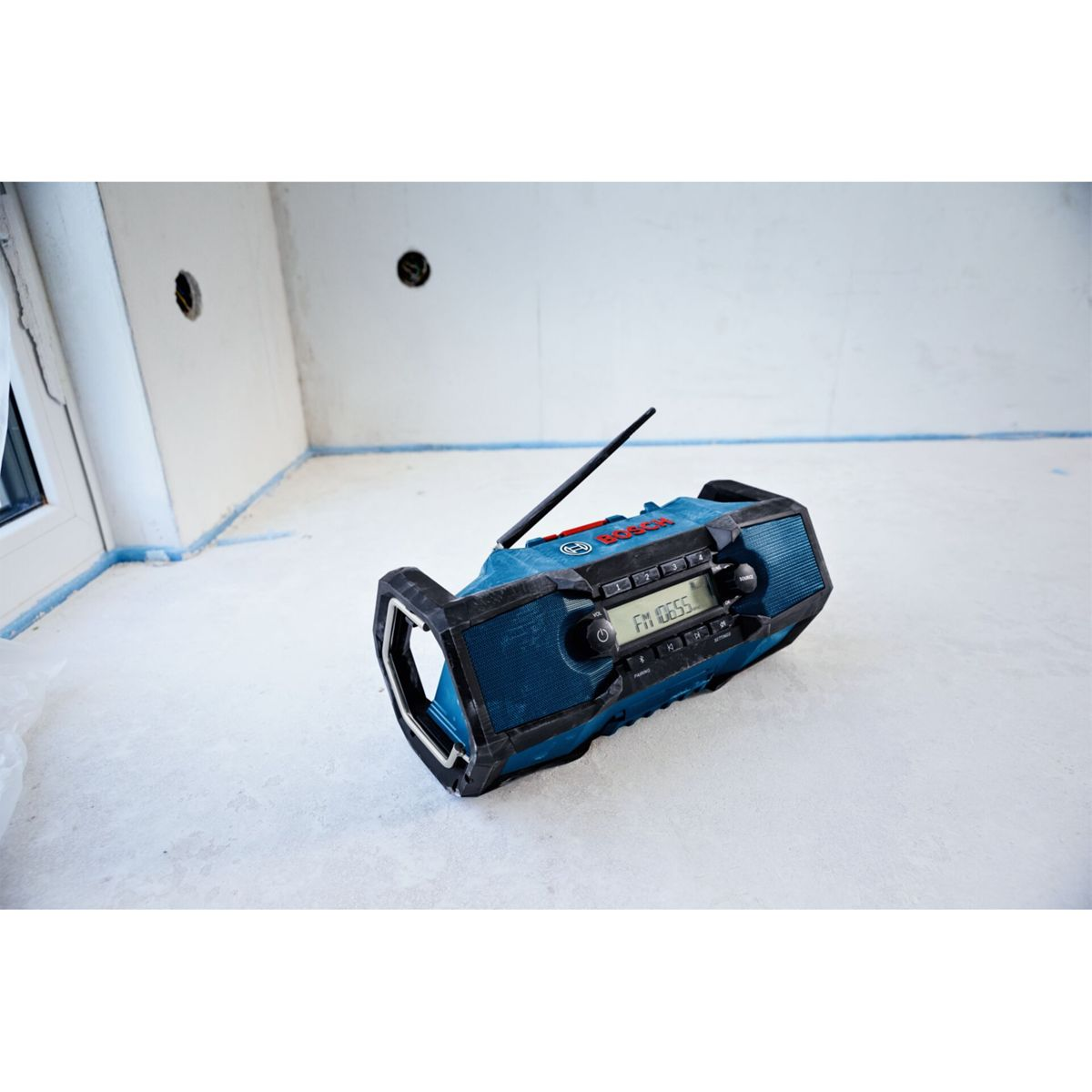 Ein blauer Bosch-Baustellenradio mit Antenne steht auf einem hellen Boden.