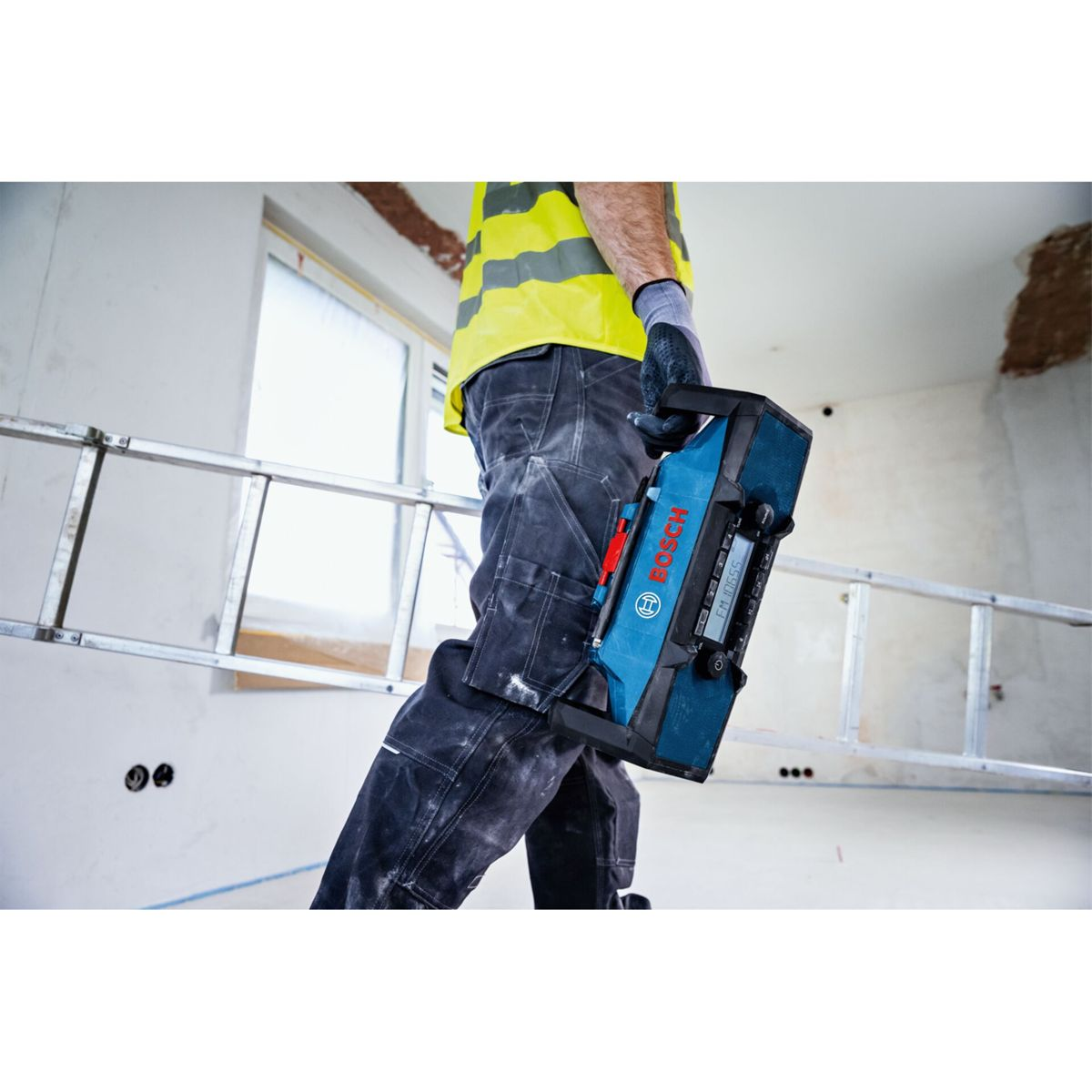 Mann mit gelber Weste hält blaues Bosch Radio auf Baustelle mit Leiter.