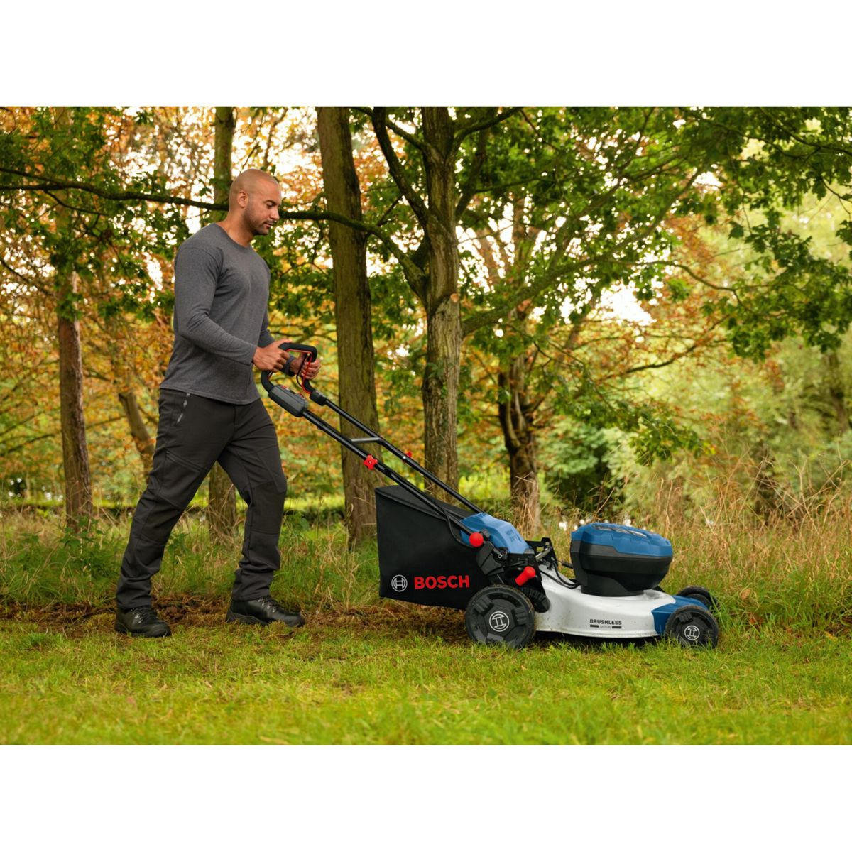 Ein Mann schiebt einen Bosch Rasenmäher durch einen herbstlichen Garten.