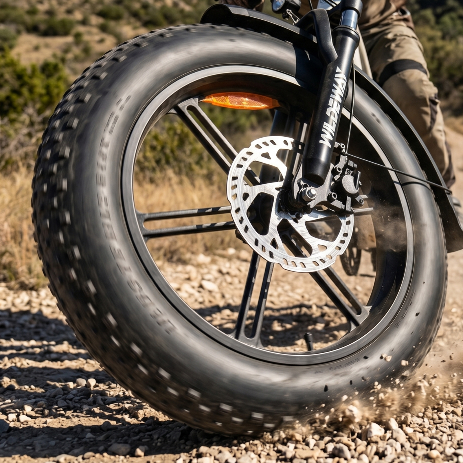 Nahaufnahme eines Fatbike-Rads, das auf einem Schotterweg Staub aufwirbelt.