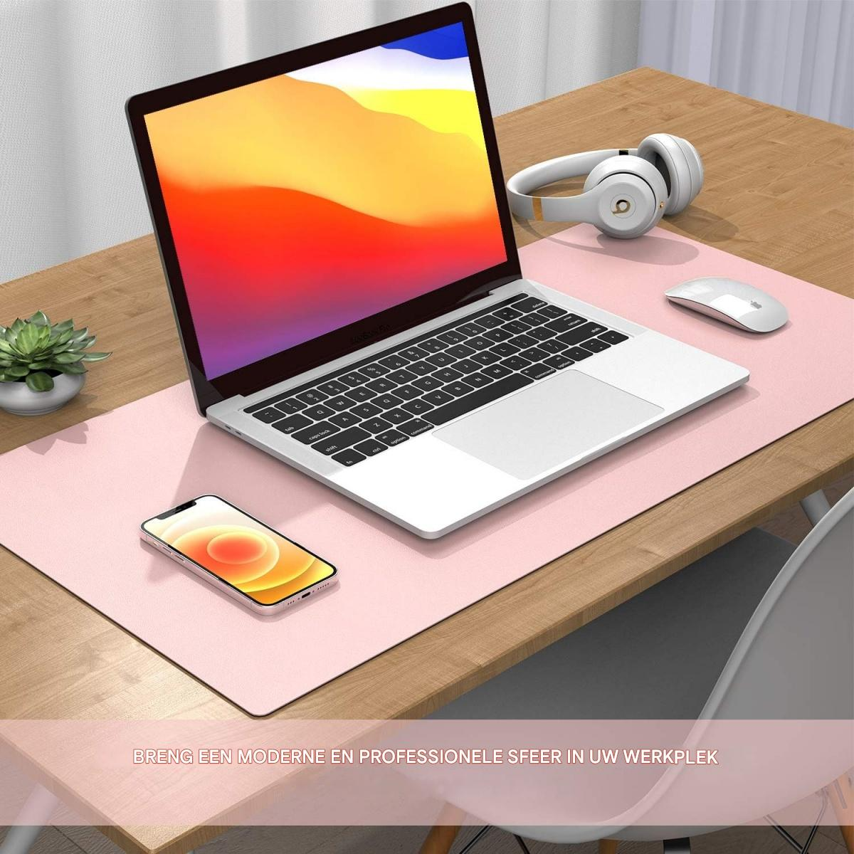 Ein Laptop, Handy, Kopfhörer und Maus auf einem rosa Pad auf einem Holztisch.