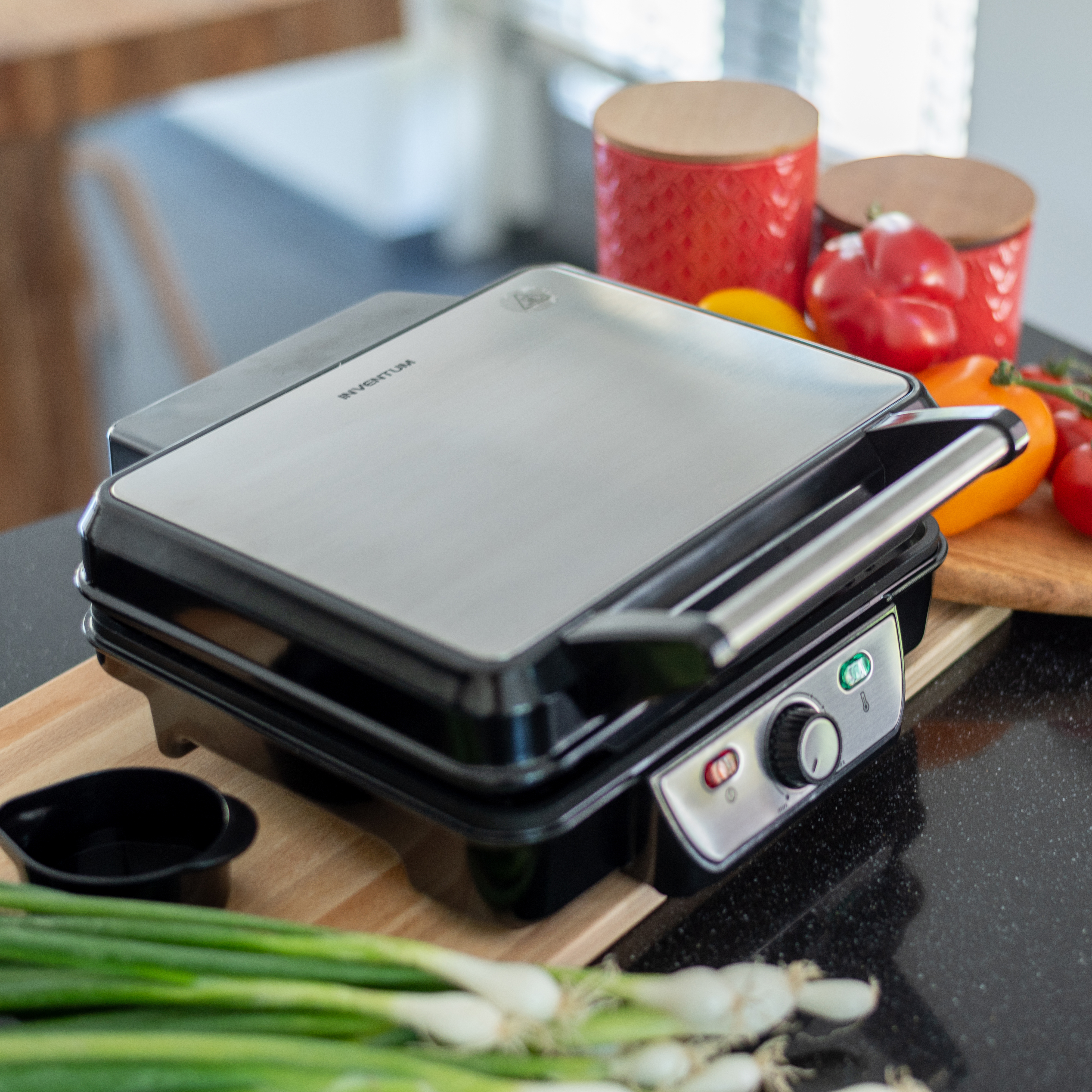 A silver contact grill with a black housing sits on a wooden countertop.