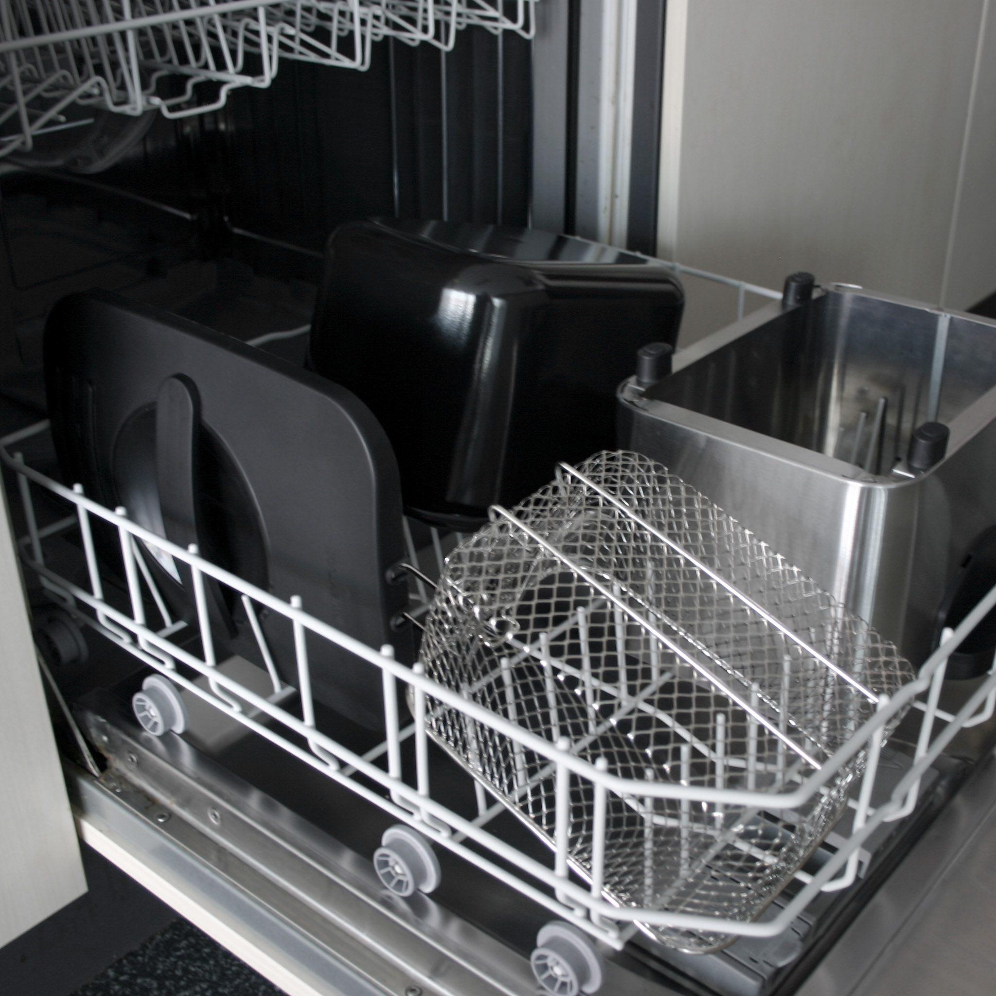 An open dishwasher with a metal basket and black parts inside.