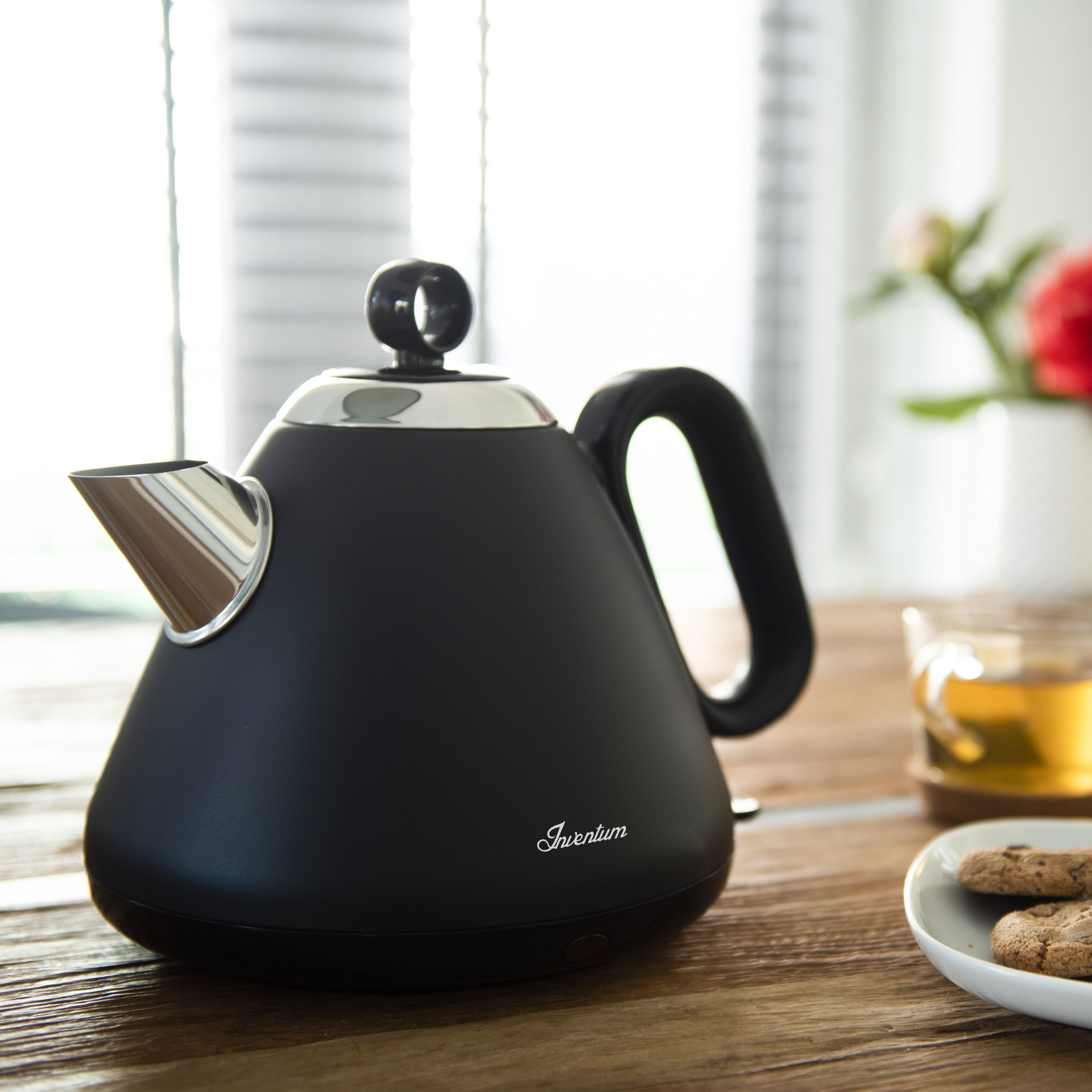 Black kettle with handle and spout next to a glass of tea and cookies.