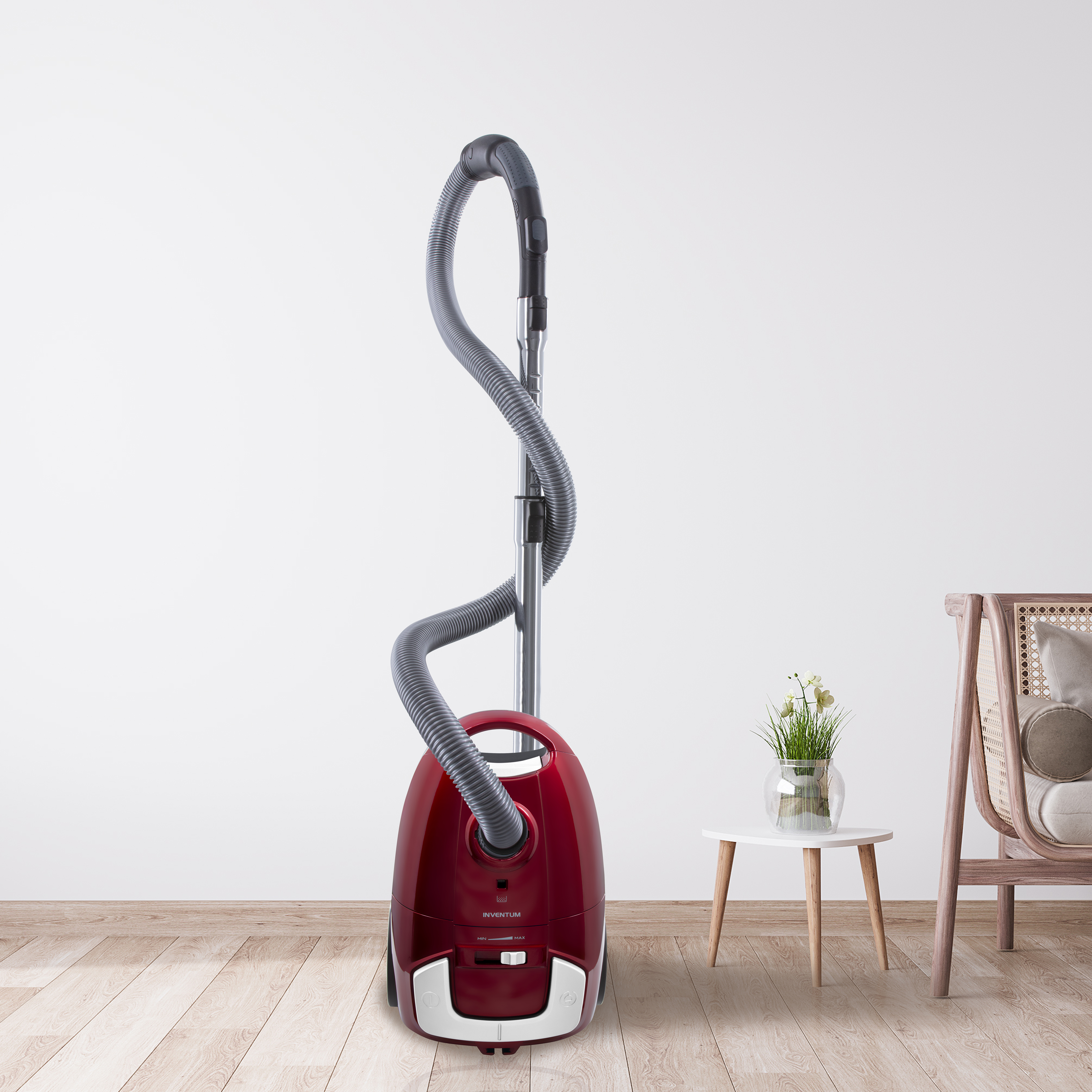 A red vacuum cleaner stands next to a small white table with a vase of flowers.