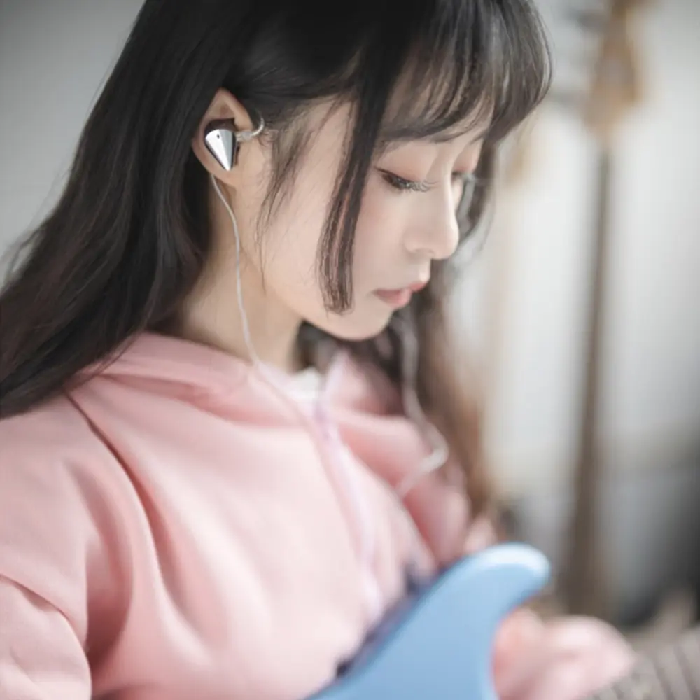 Une jeune femme en sweat à capuche rose porte des écouteurs et tient une guitare bleue.