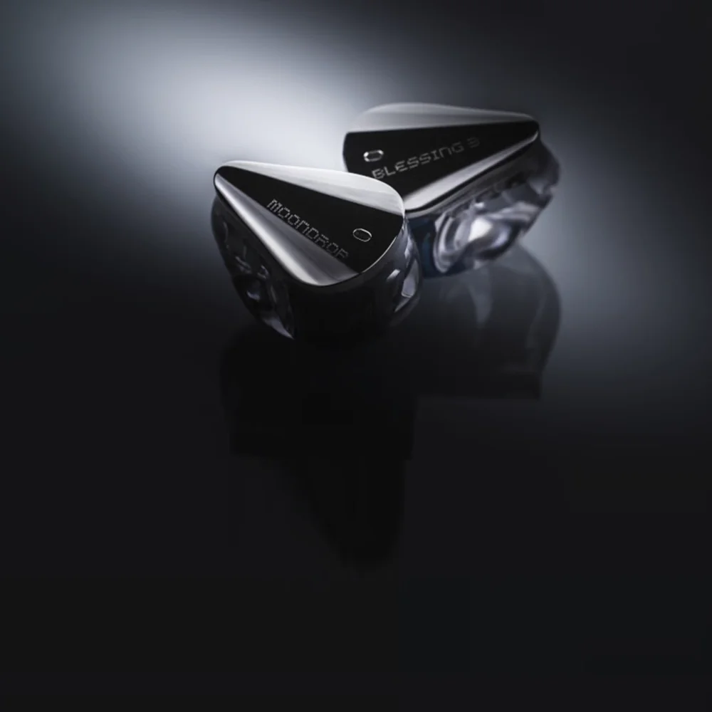 Deux écouteurs noirs Moondrop Blessing 3 avec accents clairs sur une surface sombre et réfléchissante.