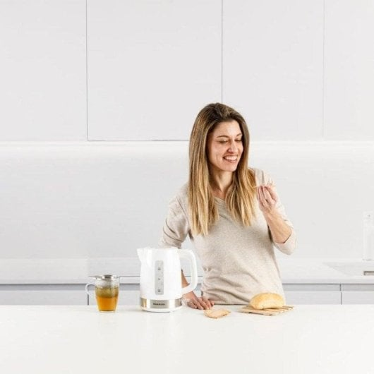 Una donna è in piedi in una cucina accanto a un bollitore e una tazza di tè.
