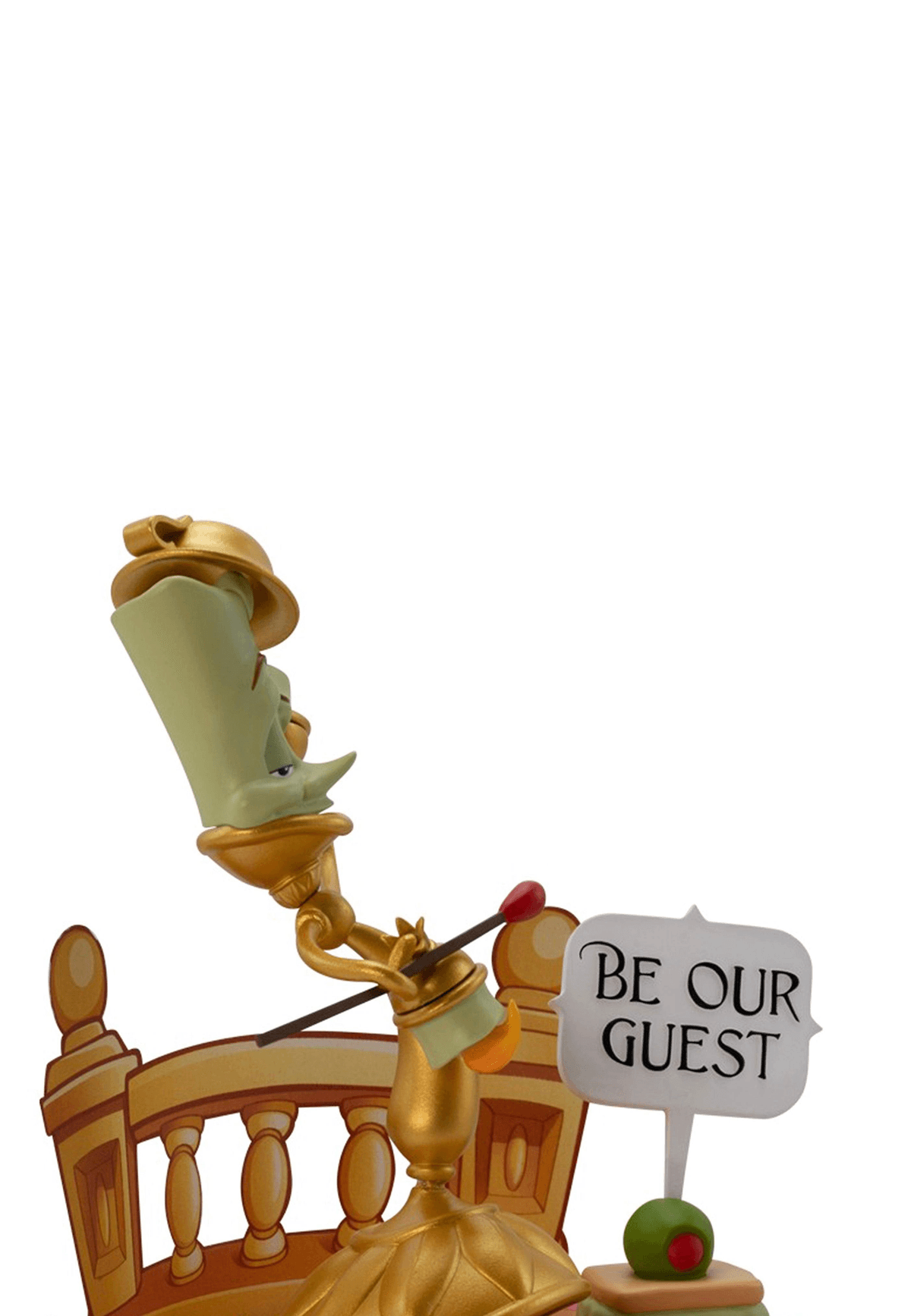 Una figura de candelabro dorado con cara verde, sosteniendo un letrero que dice 'BE OUR GUEST'.