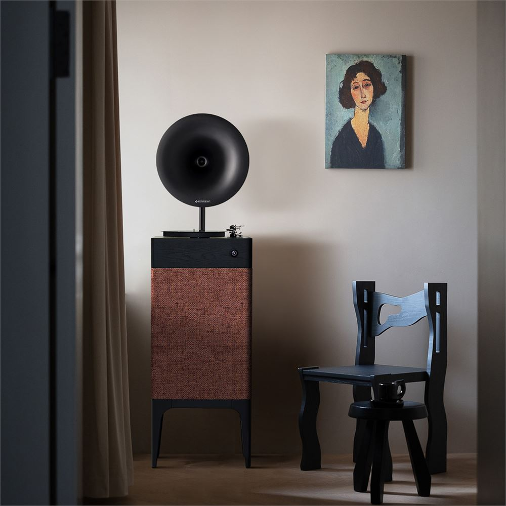Kumaş önlü bir kaide üzerinde gramofon, yanında siyah sandalye ve tablo.