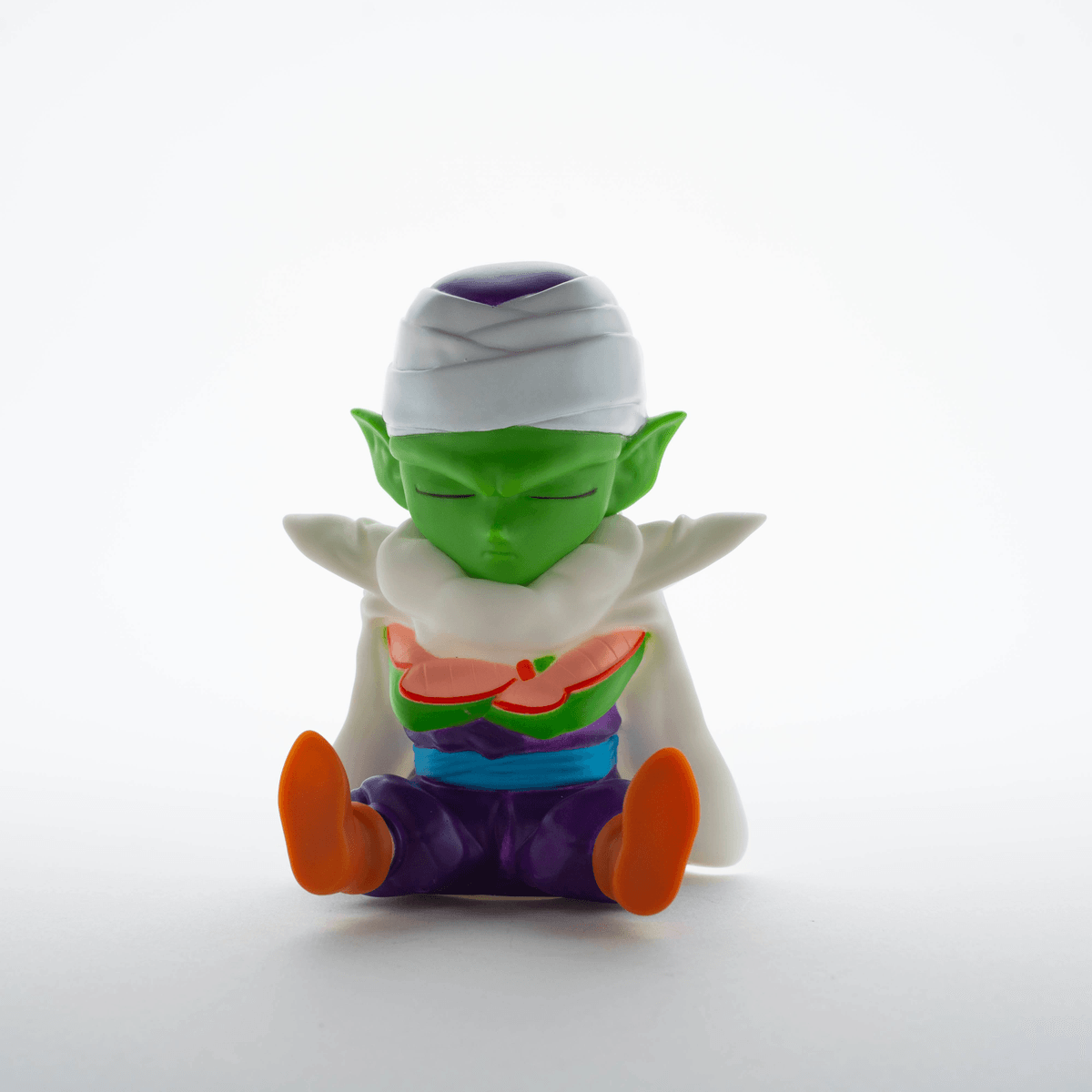 Eine grüne Figur mit geschlossenen Augen sitzt mit weißen Kleidern und orangefarbenen Füßen.