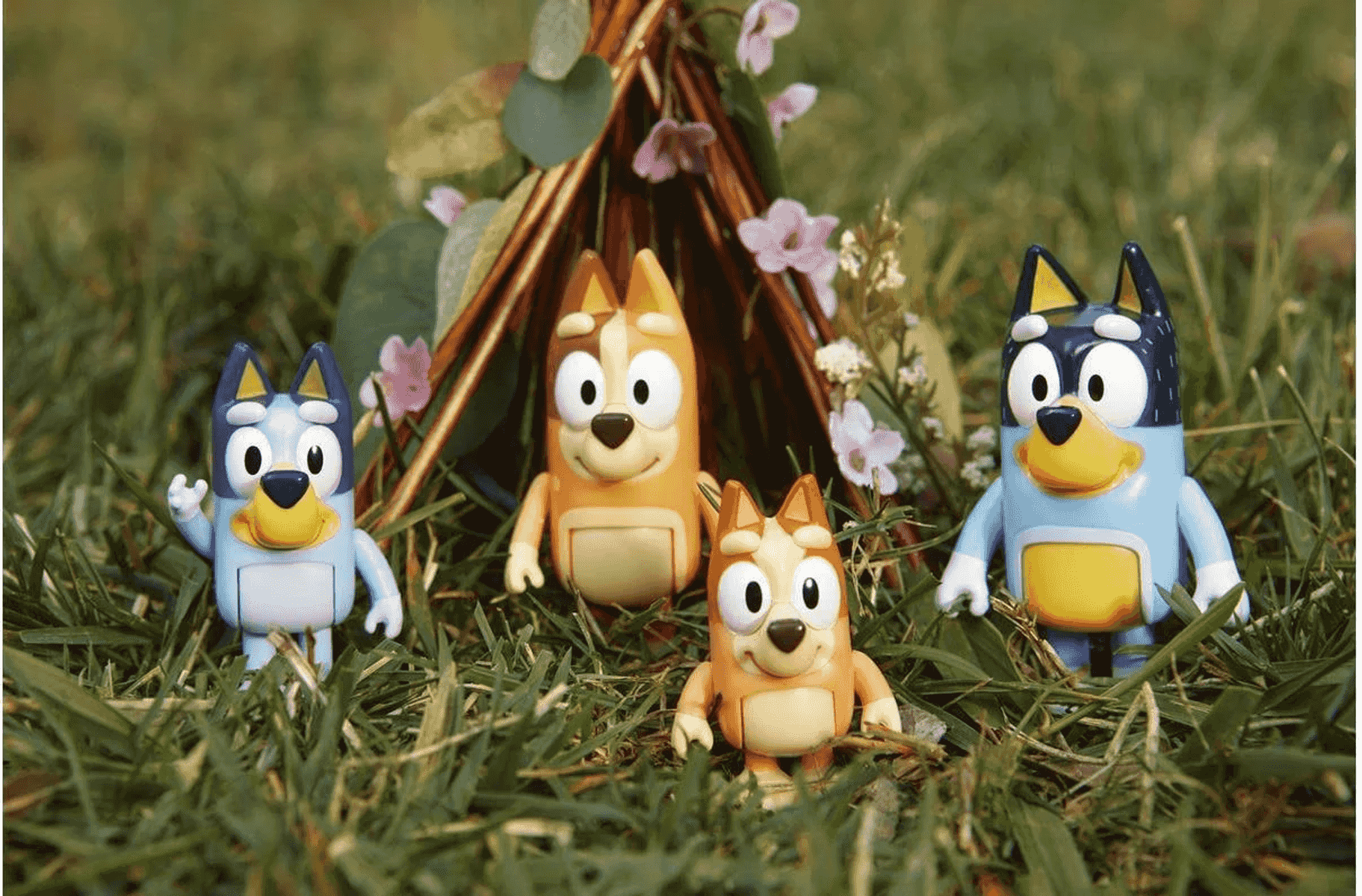 Quatre figurines Bluey se tiennent dans l'herbe devant une petite hutte avec des fleurs.