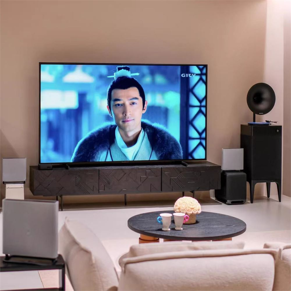 Asya kostümlü bir adam TV ekranında, hoparlörlerle çevrili.