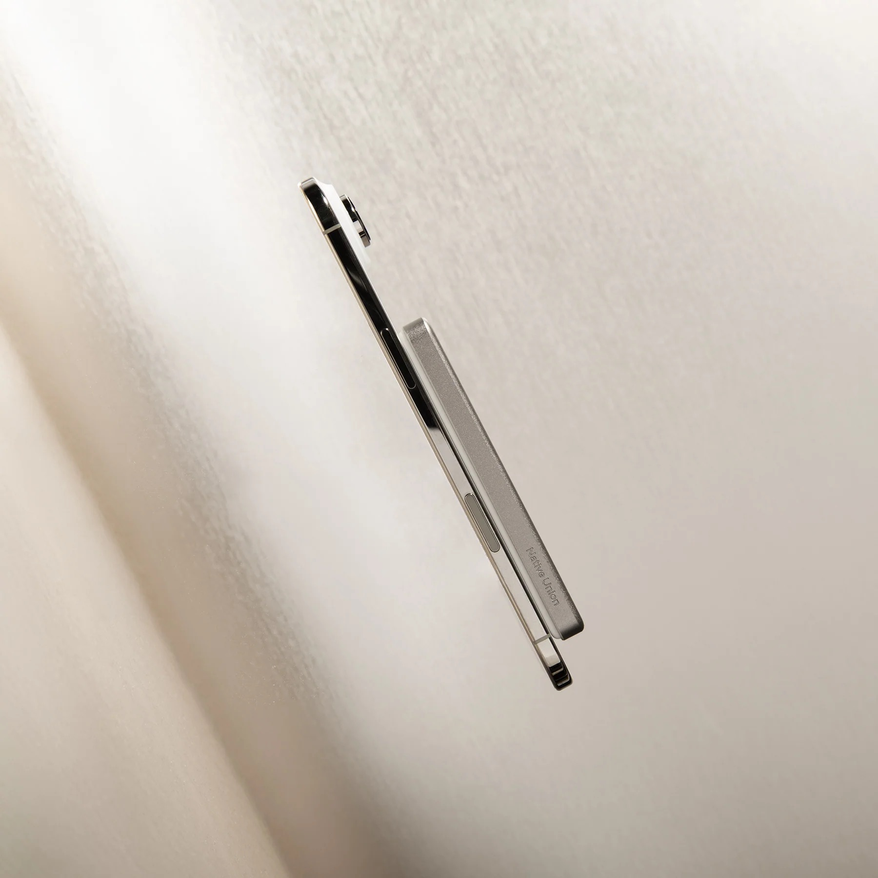 Un smartphone argenté avec un étui repose sur un tissu blanc drapé.