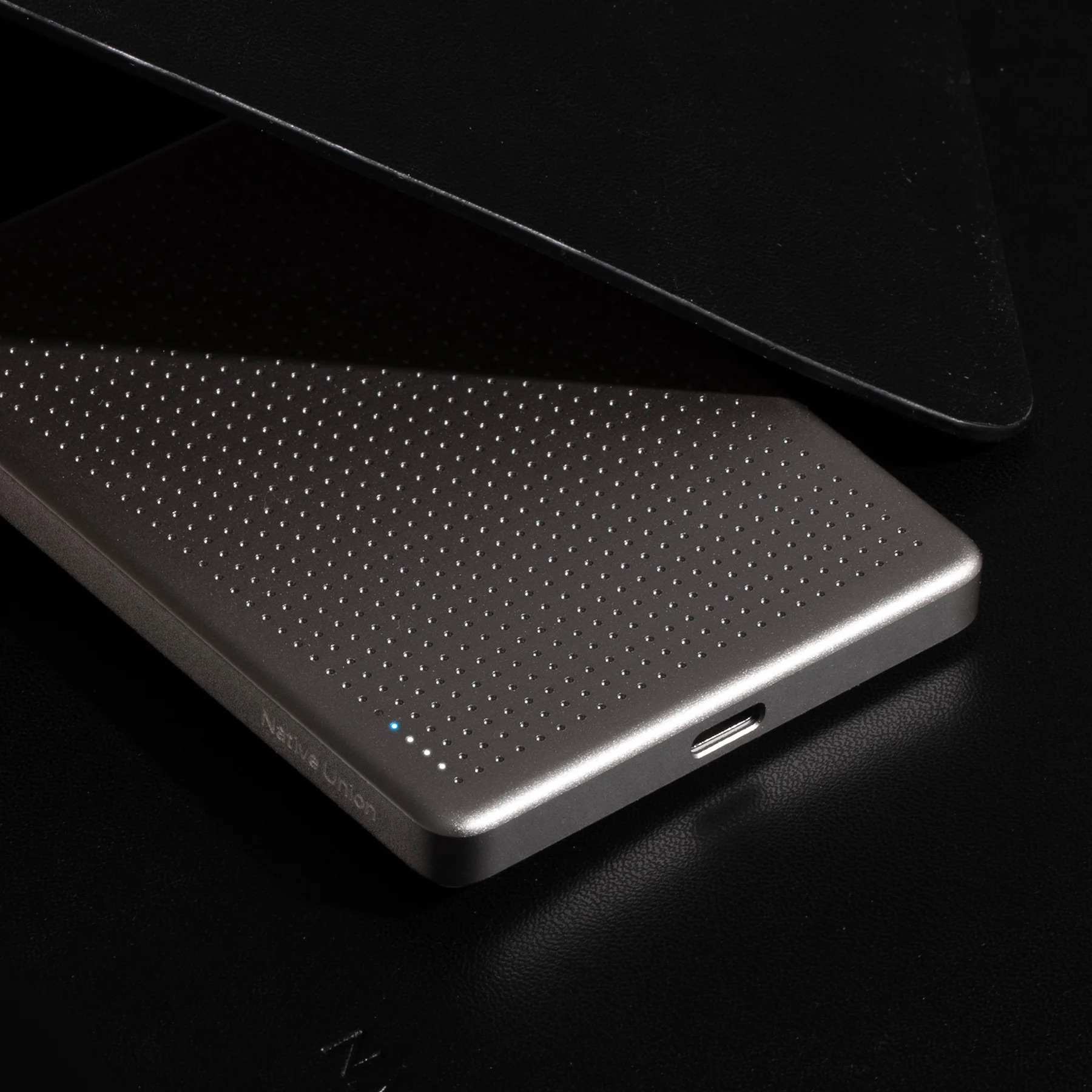Une batterie externe argentée à surface perforée repose sur une texture noire.