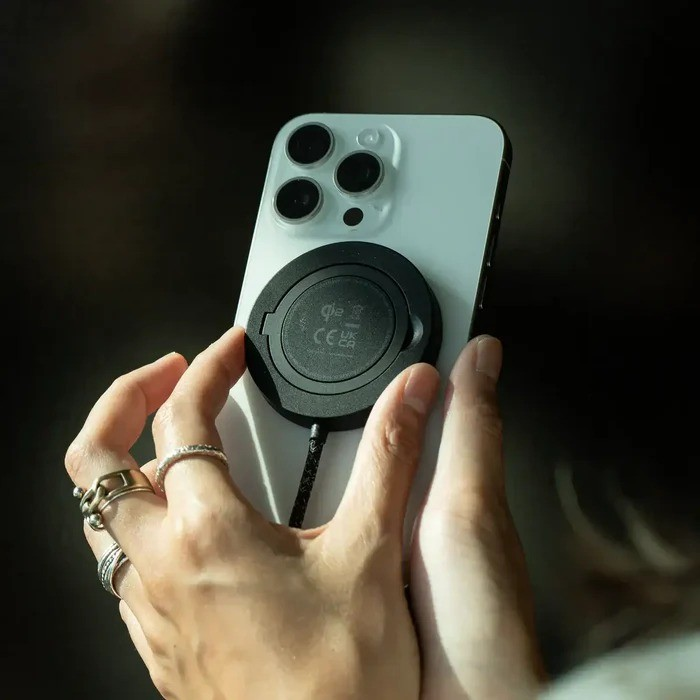 Una persona sostiene un smartphone blanco con un disco de carga magnético negro en la parte posterior.