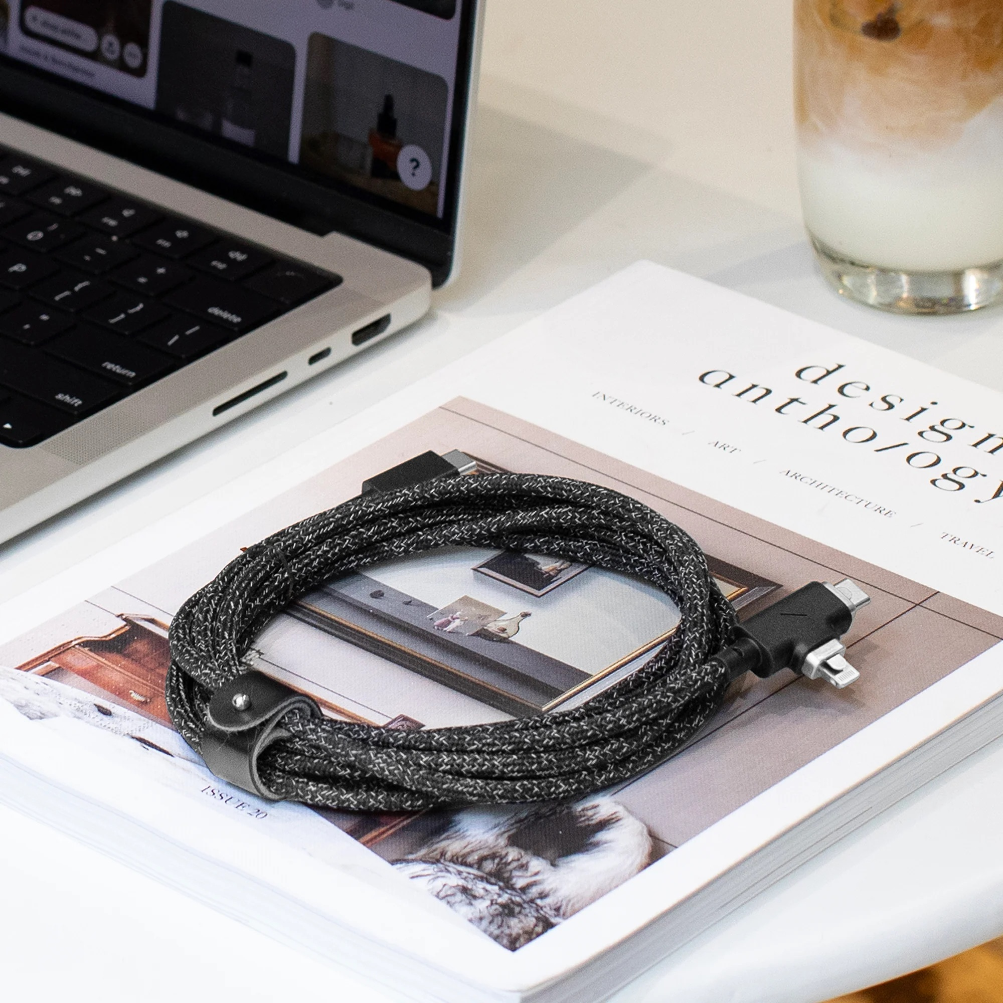 Un câble tressé noir et blanc enroulé avec des connecteurs USB-C et Lightning repose sur un magazine.