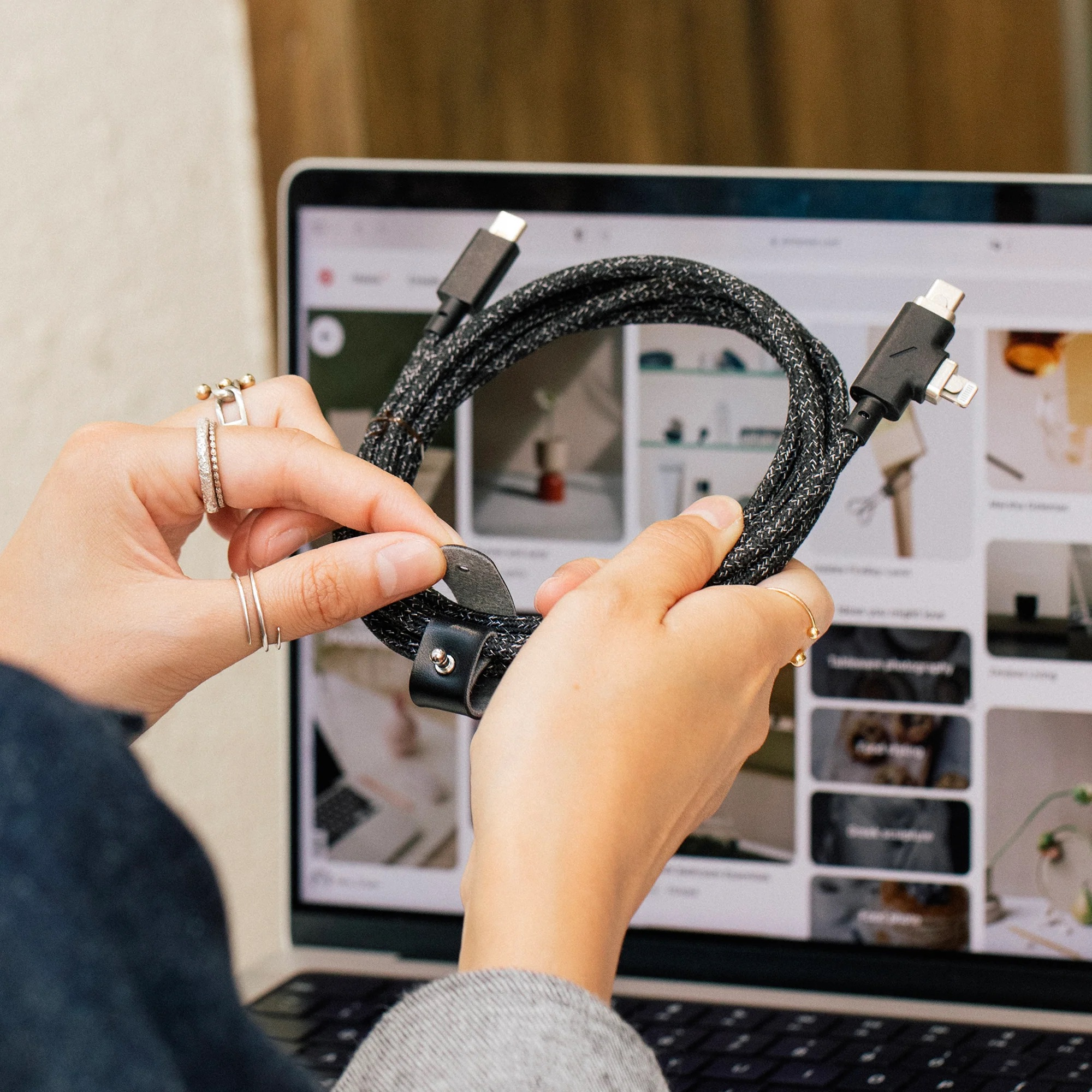Une personne tient un câble tressé avec des connecteurs USB-C et Lightning devant un ordinateur portable.