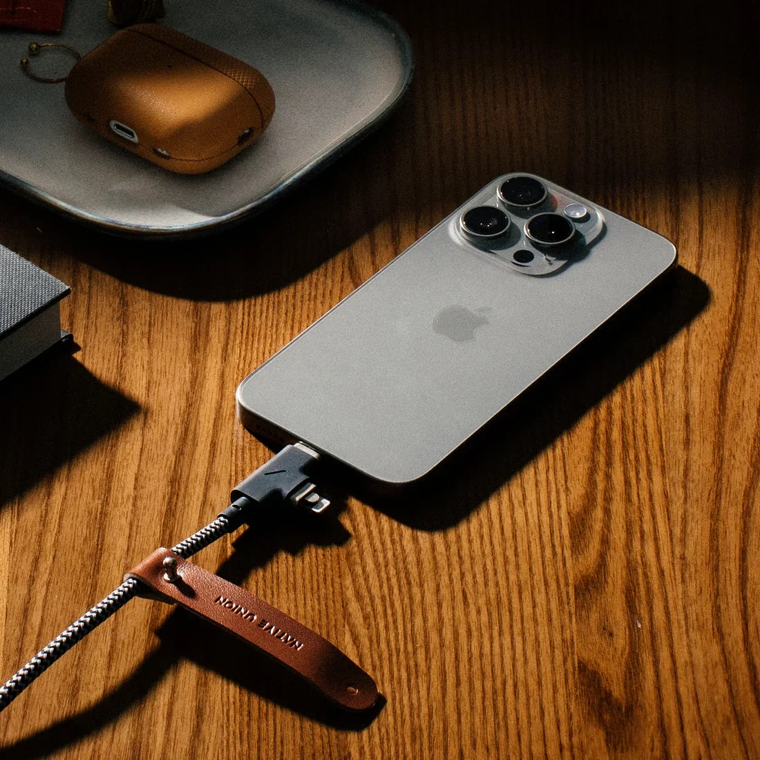 iPhone argento in carica con cavo dotato di cinturino in pelle marrone.