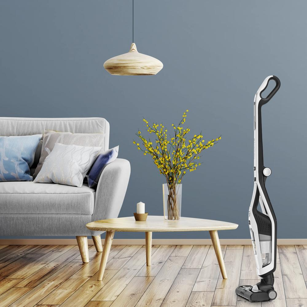 Un área de sala de estar moderna con sofá, mesa de centro, jarrón con flores amarillas y aspiradora.