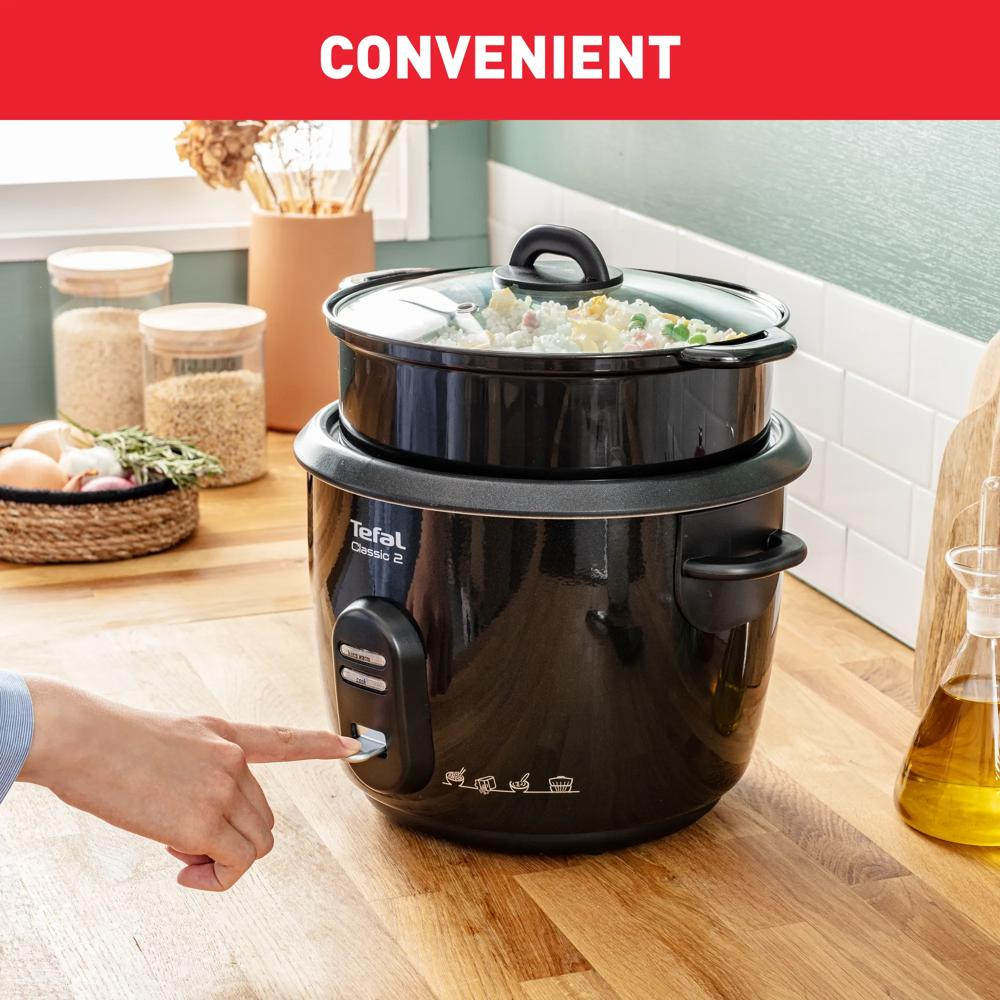 Eine Person drückt einen Knopf an einem schwarzen Tefal-Reiskocher mit Essen darin.