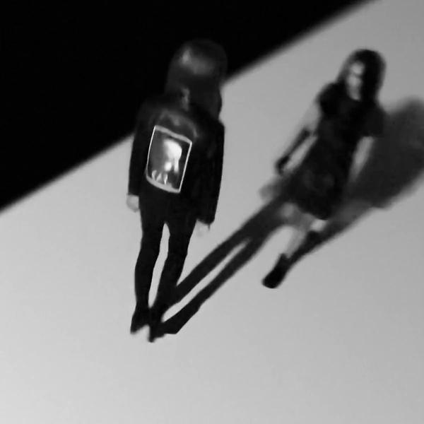 Due figure in ombra stanno in piedi, una con una giacca con un quadro.