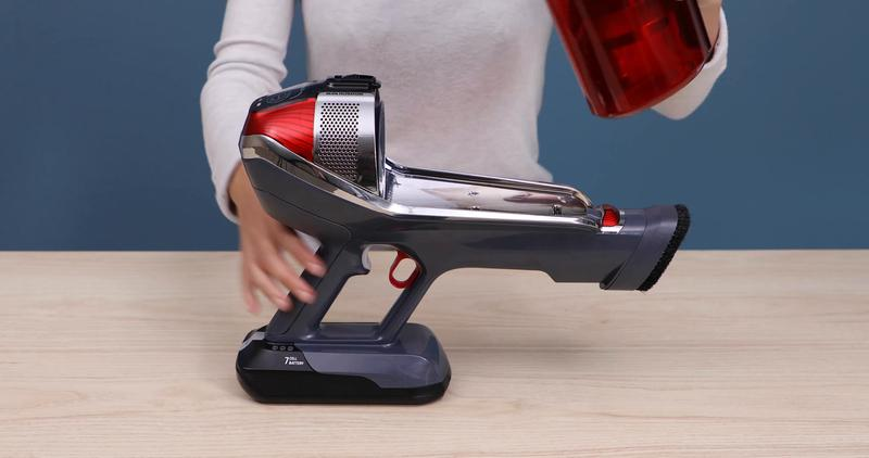 Persona sujeta un recipiente rojo sobre una aspiradora inalámbrica gris.